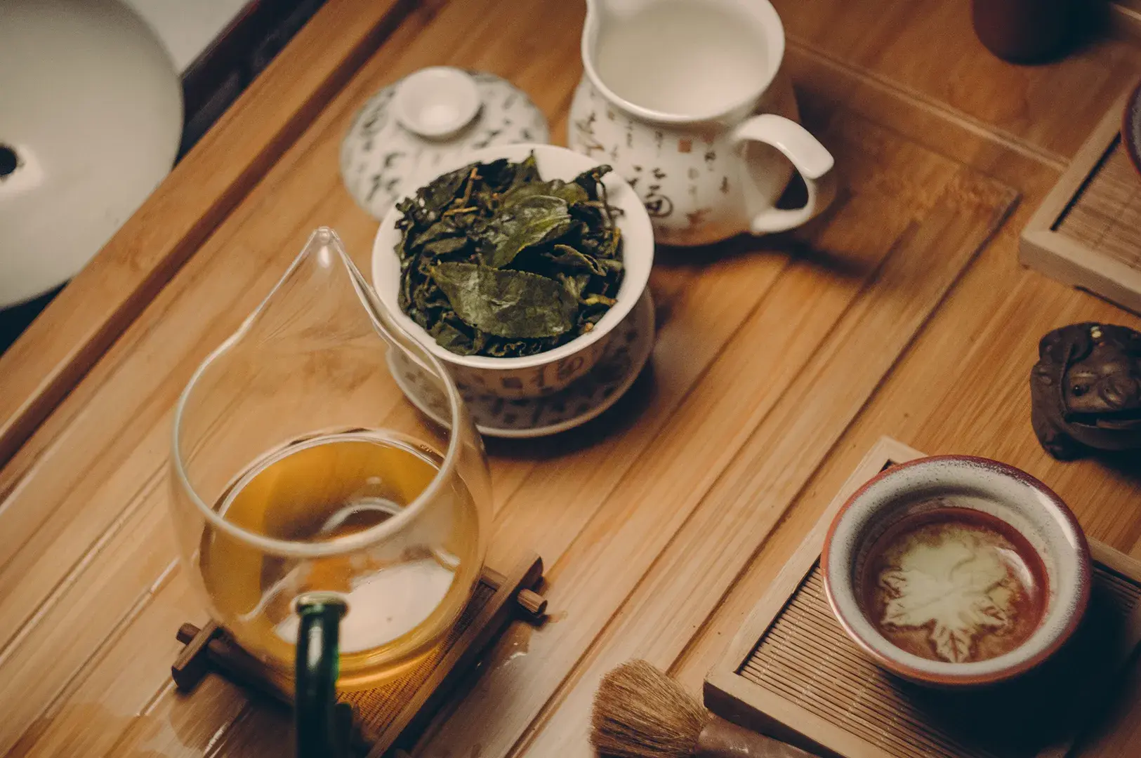 Gong fu tea set with steeped leaves in a gaiwan and golden tea in a clear pitcher.