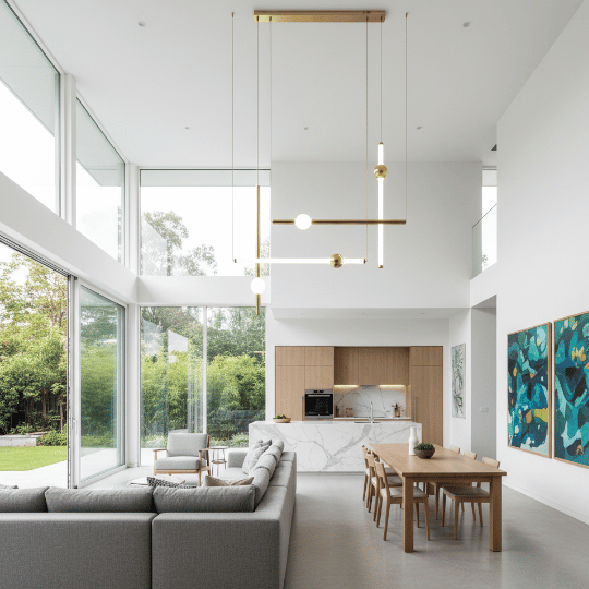 Linear brass pendant light with exposed bulbs suspended in a double-height open living and dining space.