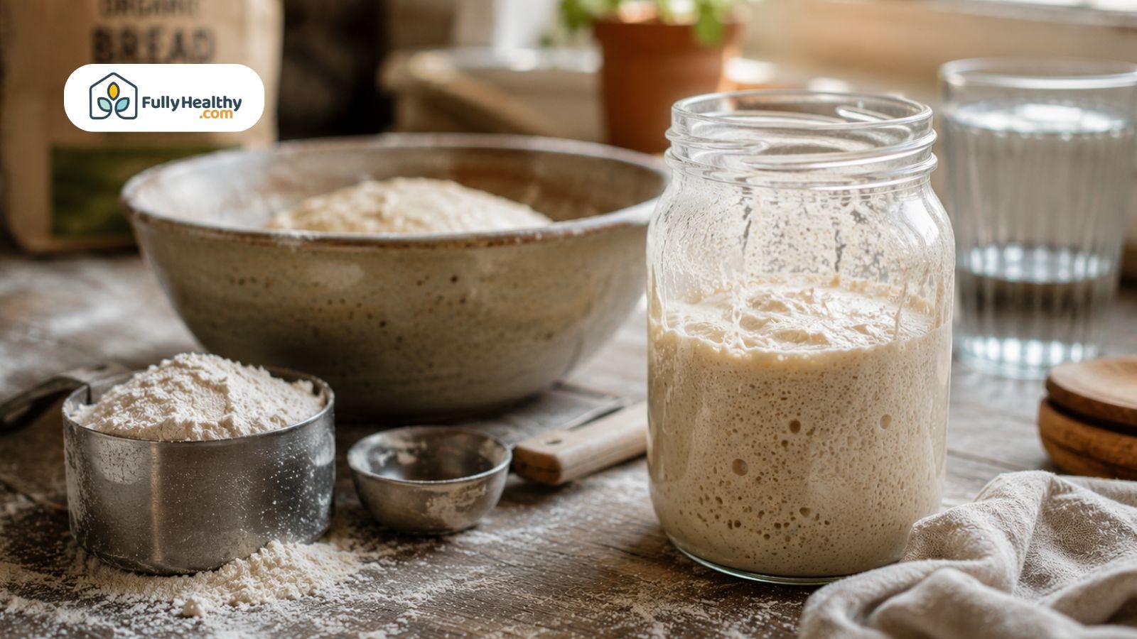 Active sourdough starter in a glass jar beside flour and baking ingredients on a kitchen counter.