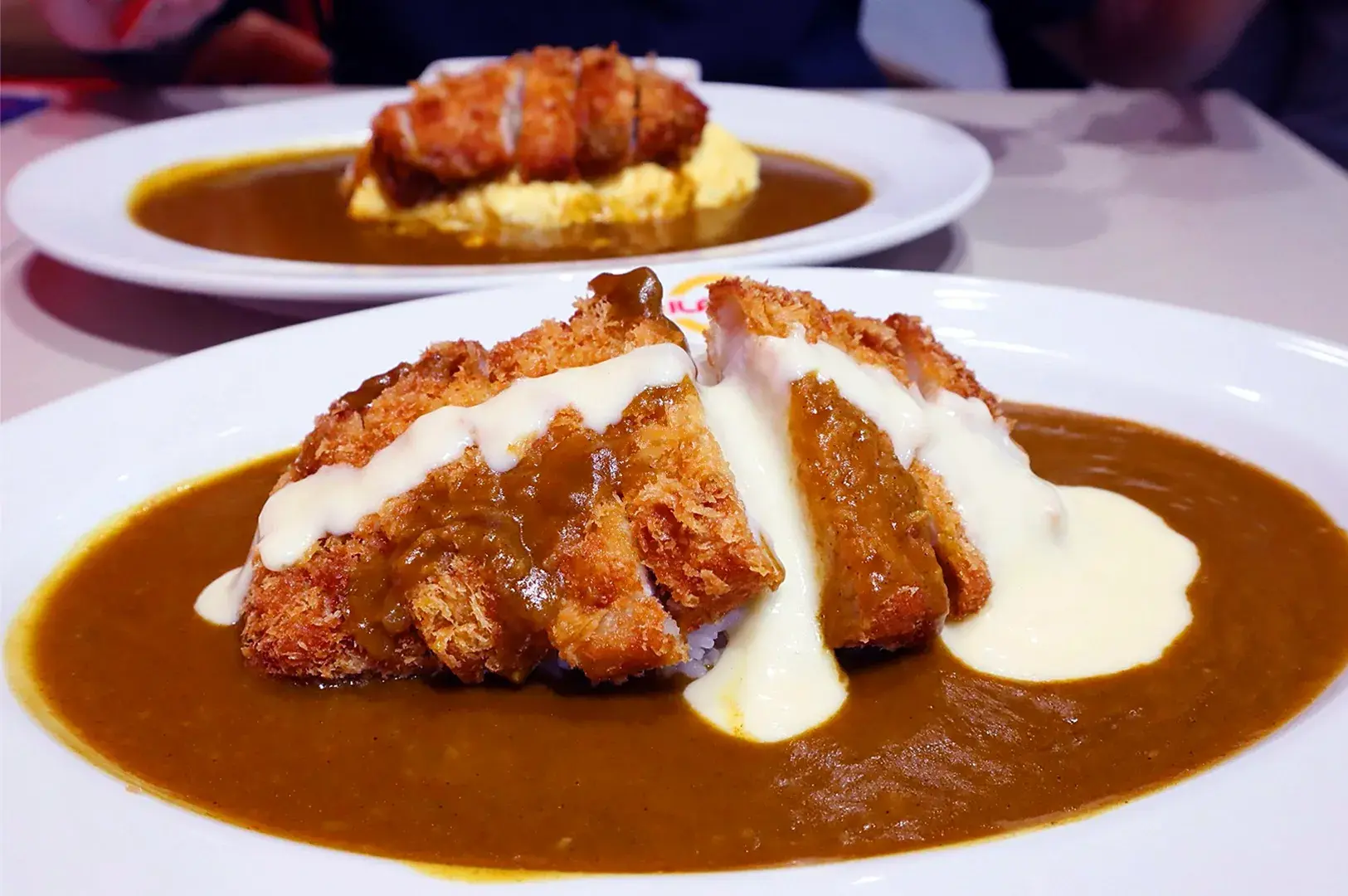 Close-up food photo of Japanese beef curry rice served in a white bowl, featuring tender beef chunks in rich brown curry sauce alongside steamed white rice topped with chili flakes.