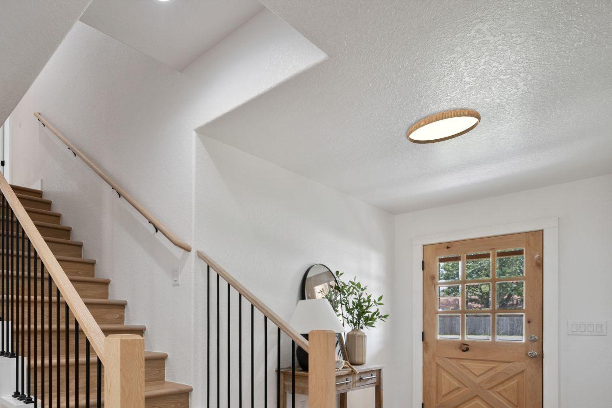 Round flush mount ceiling light with wood-tone trim illuminating a bright home entryway