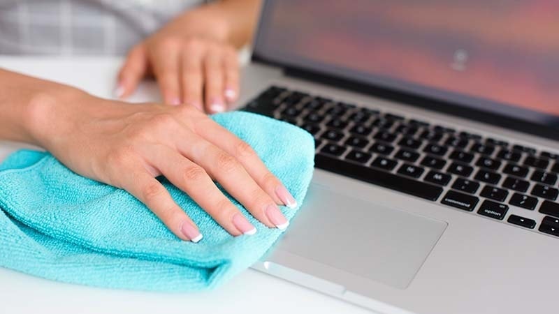 A woman using a microfiber cleaning cloth on her laptop