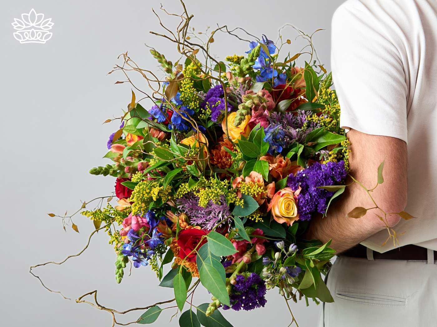 Alt text: "Man holding a lavish bouquet filled with a vibrant assortment of flowers including roses, snapdragons, and statice in a rich palette of blues, purples, oranges, and yellows, representing celebration and joy. Graduation. Delivered with Heart. Fabulous Flowers and Gifts.