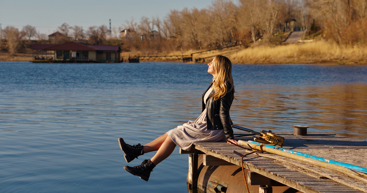 content girl resting on wooden pier and enjoying the sun to depict harmony with self