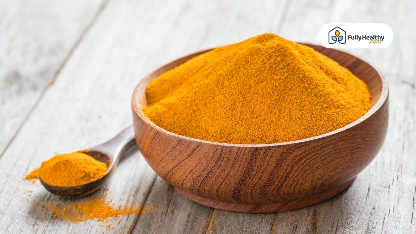 Wooden bowl and spoon filled with turmeric powder on rustic surface