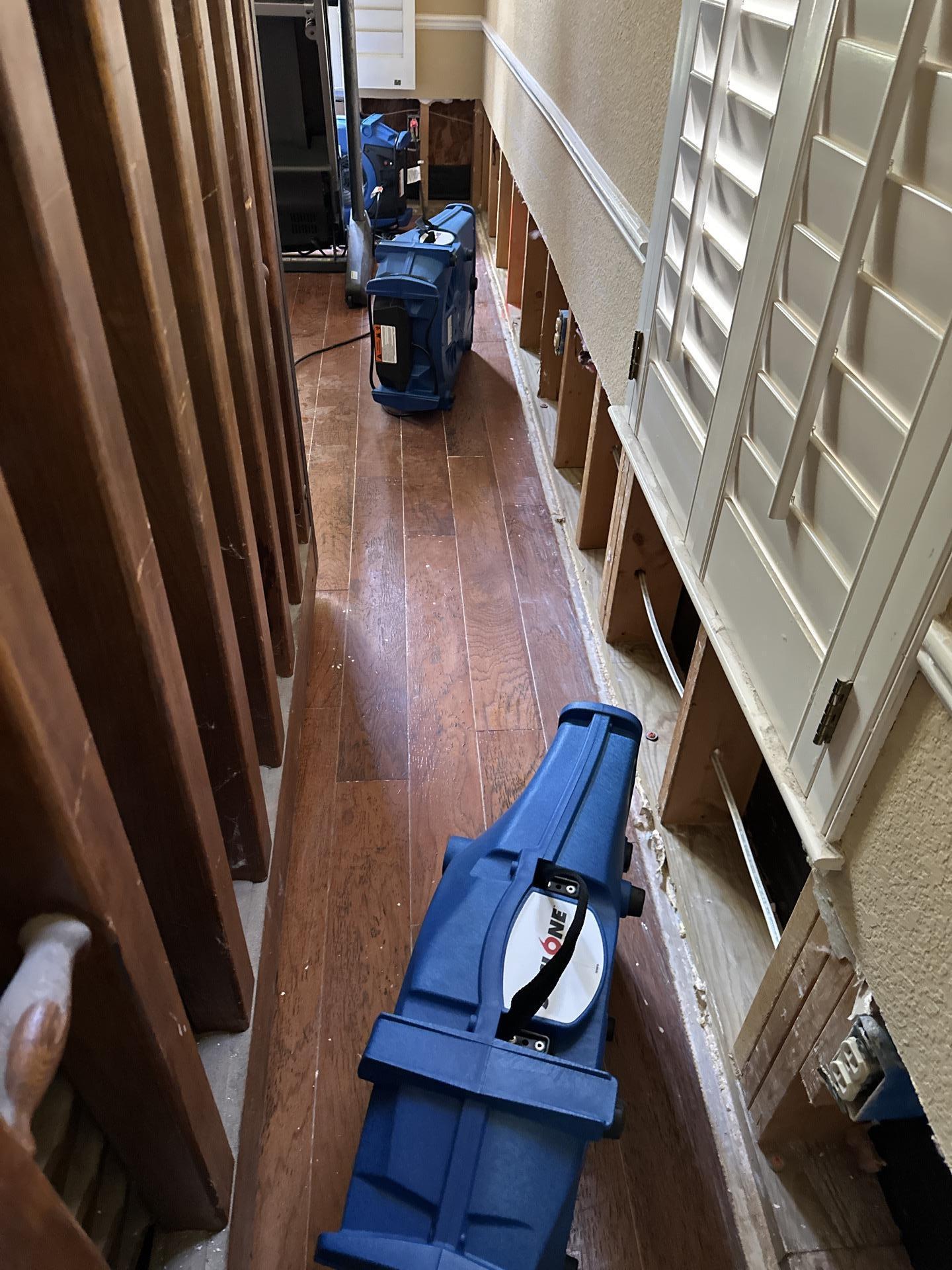 The image depicts industrial air movers and dehumidifiers actively drying a room affected by flood damage, where standing water has been removed as part of the water damage restoration process. These advanced drying equipment pieces are crucial in preventing further damage and mold growth in the affected areas.
