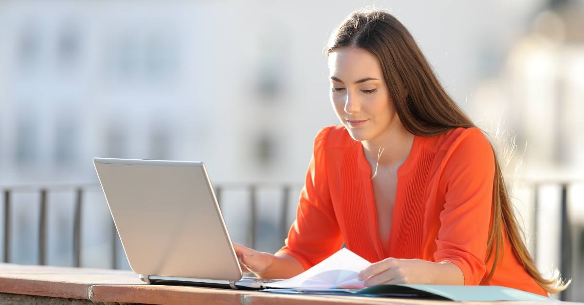 Woman utilizes the self-employed tax credit, smiling while working on her laptop outdoors.