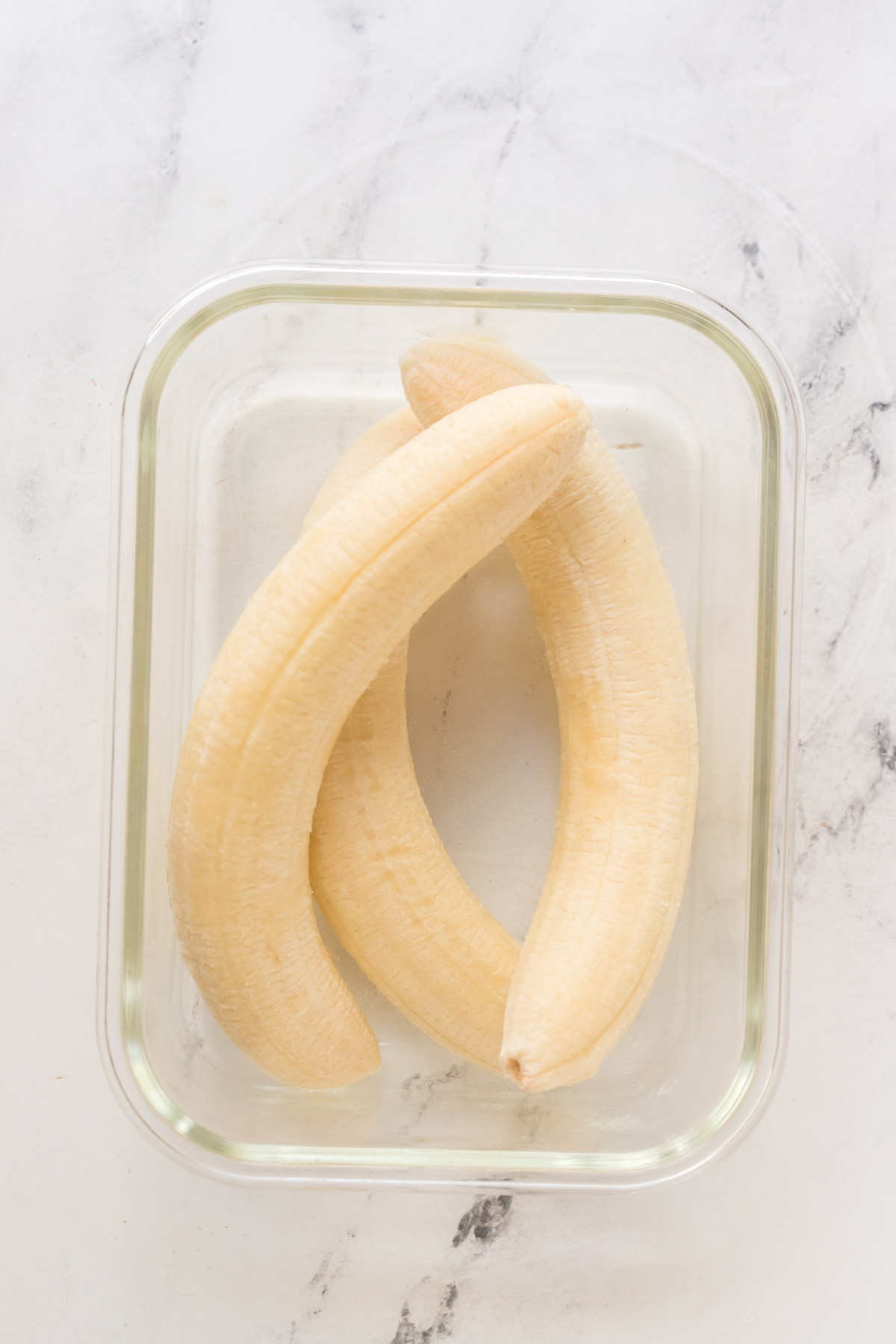 three frozen bananas in a glass container