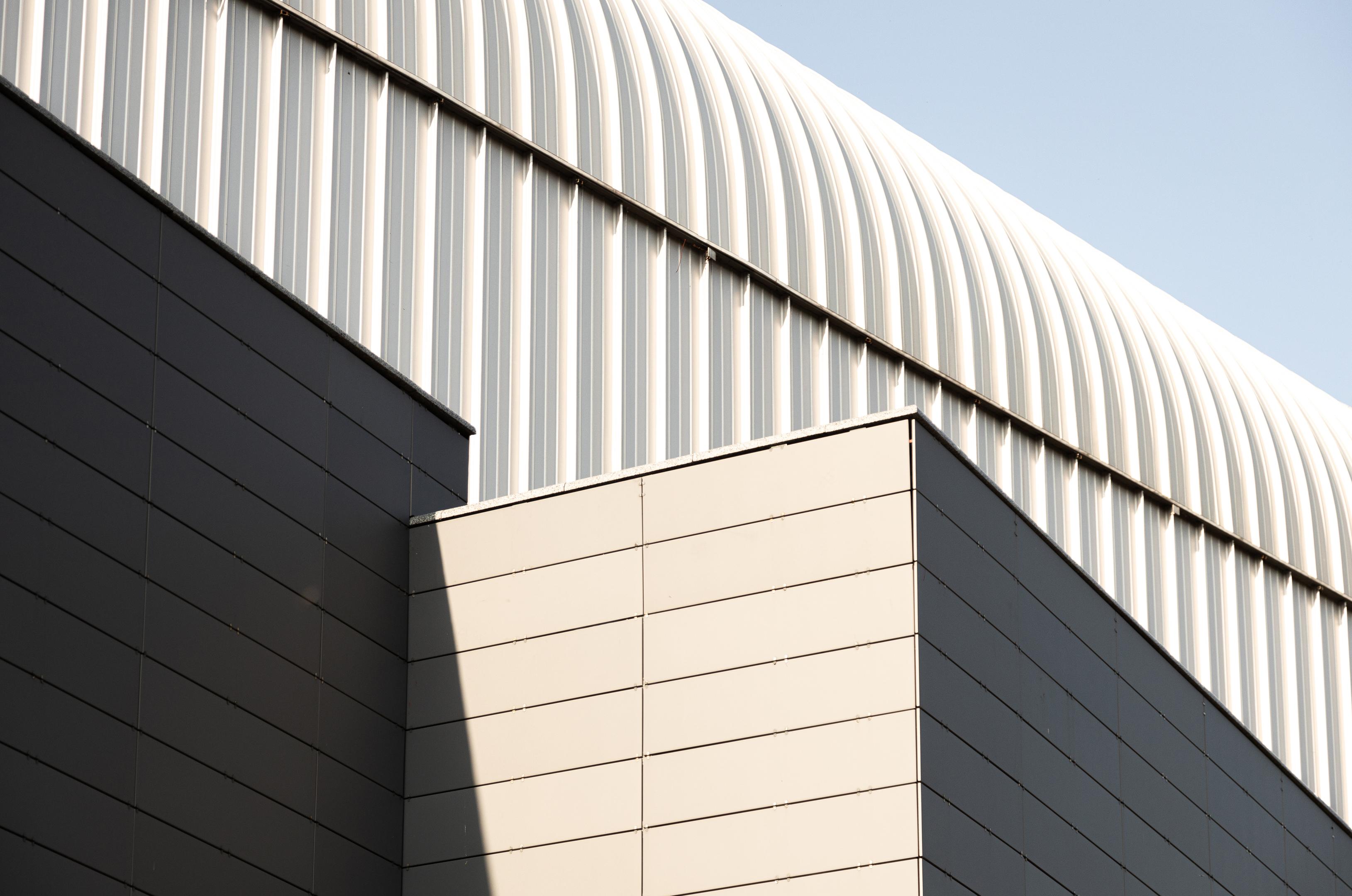 Outside view of building with metal walls and arched roof of light grey color