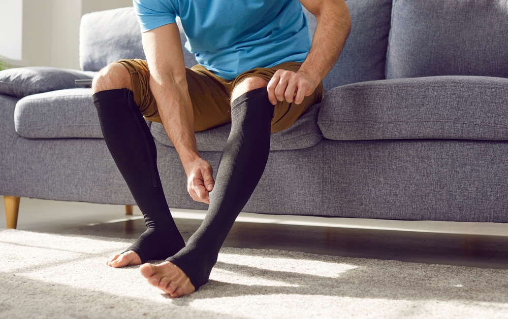 A person wearing compression stockings while sitting with their legs elevated