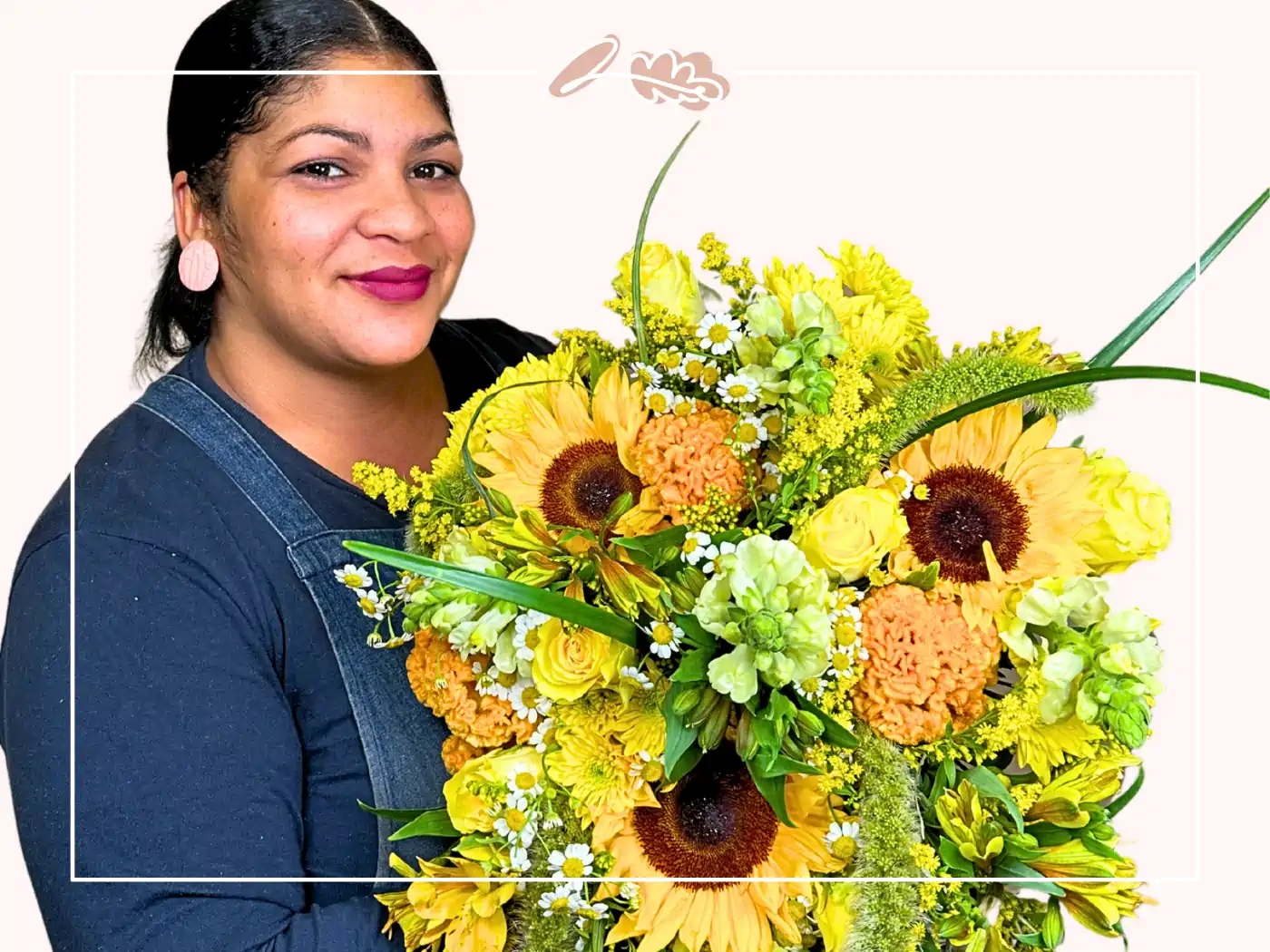 A woman with dark hair in a dark top, holding a bright bouquet of yellow sunflowers and green foliage, smiling confidently.