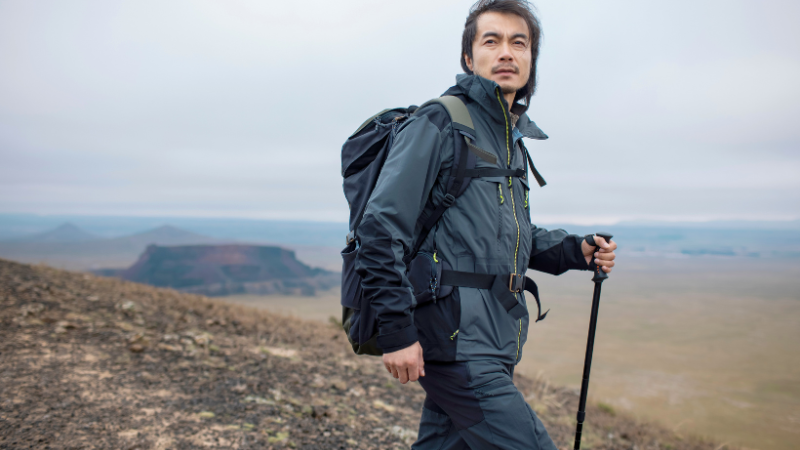 A hiker with a backpack and trekking pole ascends a rocky hillside.