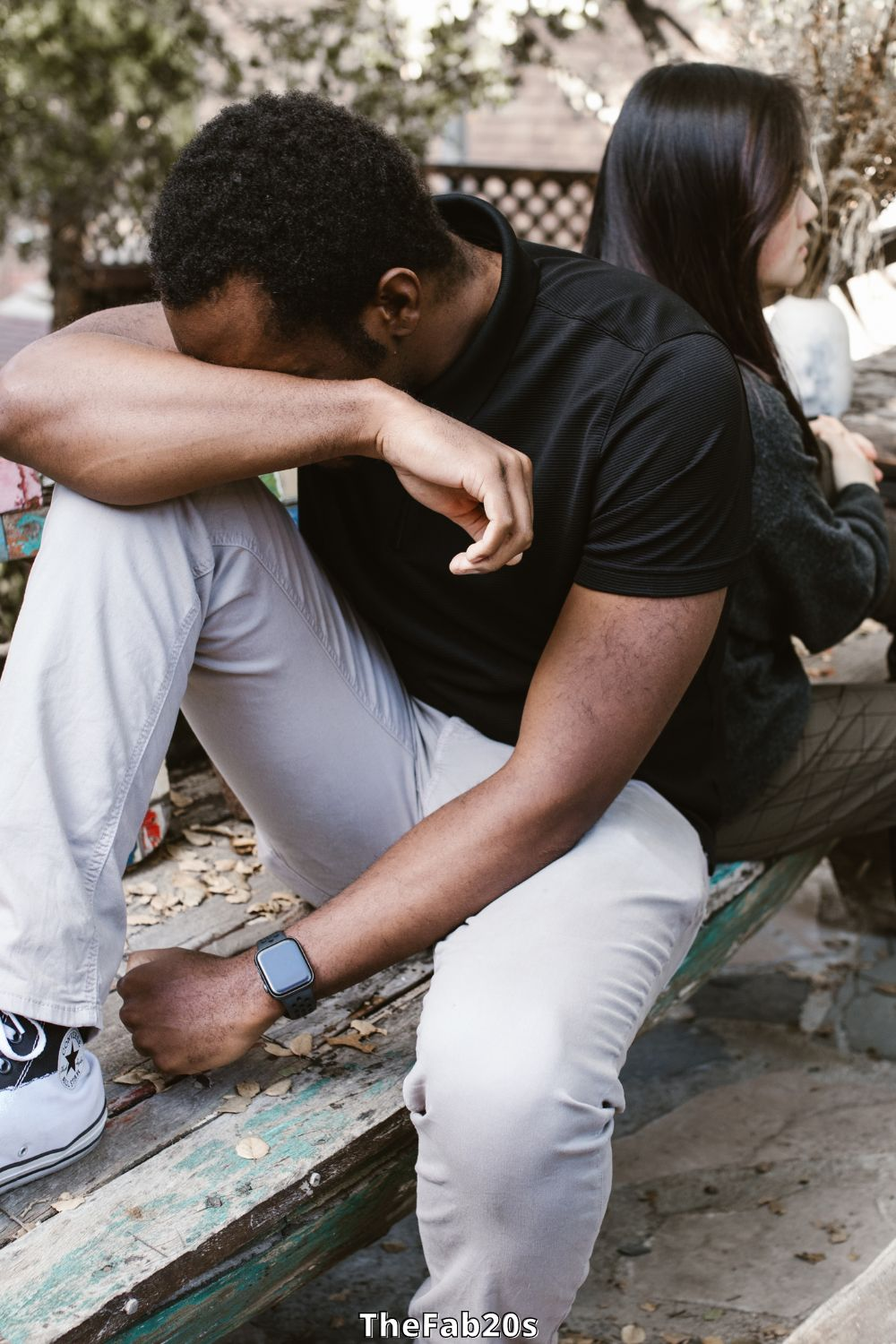 Couple sitting baack-to-back - man upset and crying into arm