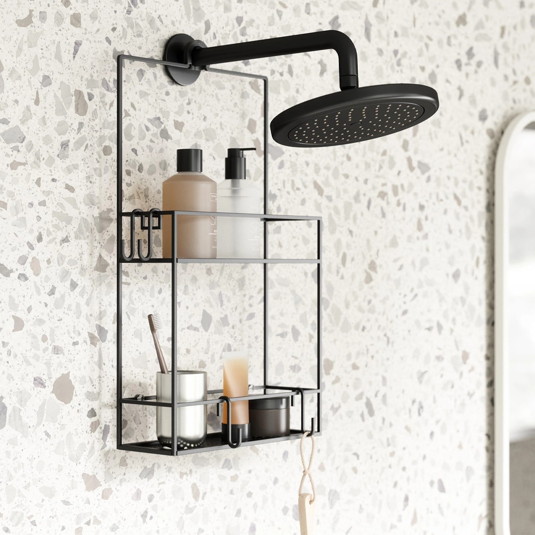 Close-up of modern shower caddy holding bathroom accessories like bottles, candles, and a toothbrush, mounted on a terrazzo wall in a contemporary bathroom.