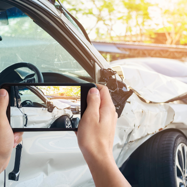 A photograph showing a person taking pictures of vehicle damage after a hit and run.