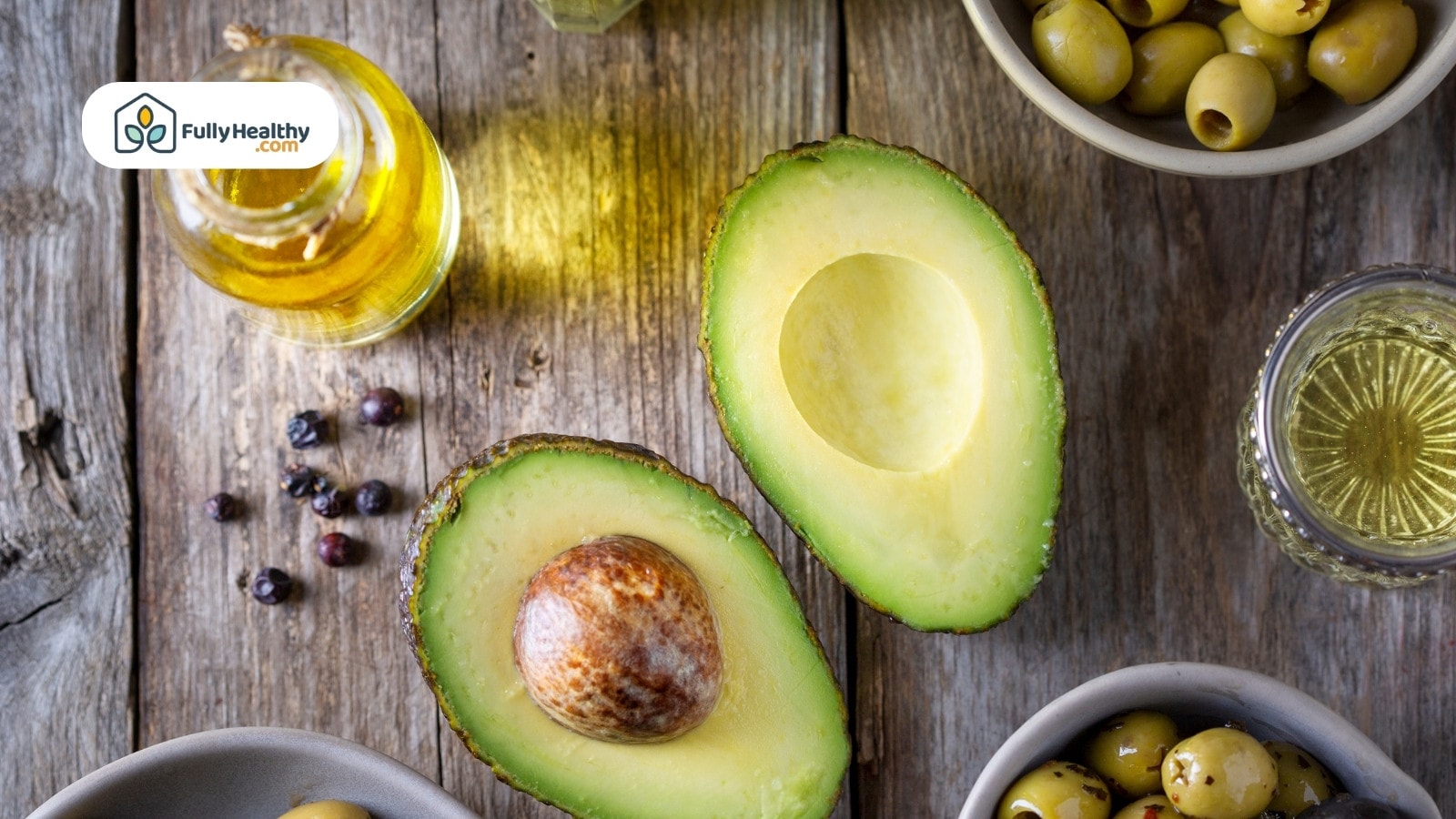 Halved avocado with bottle of oil and green olives nearby