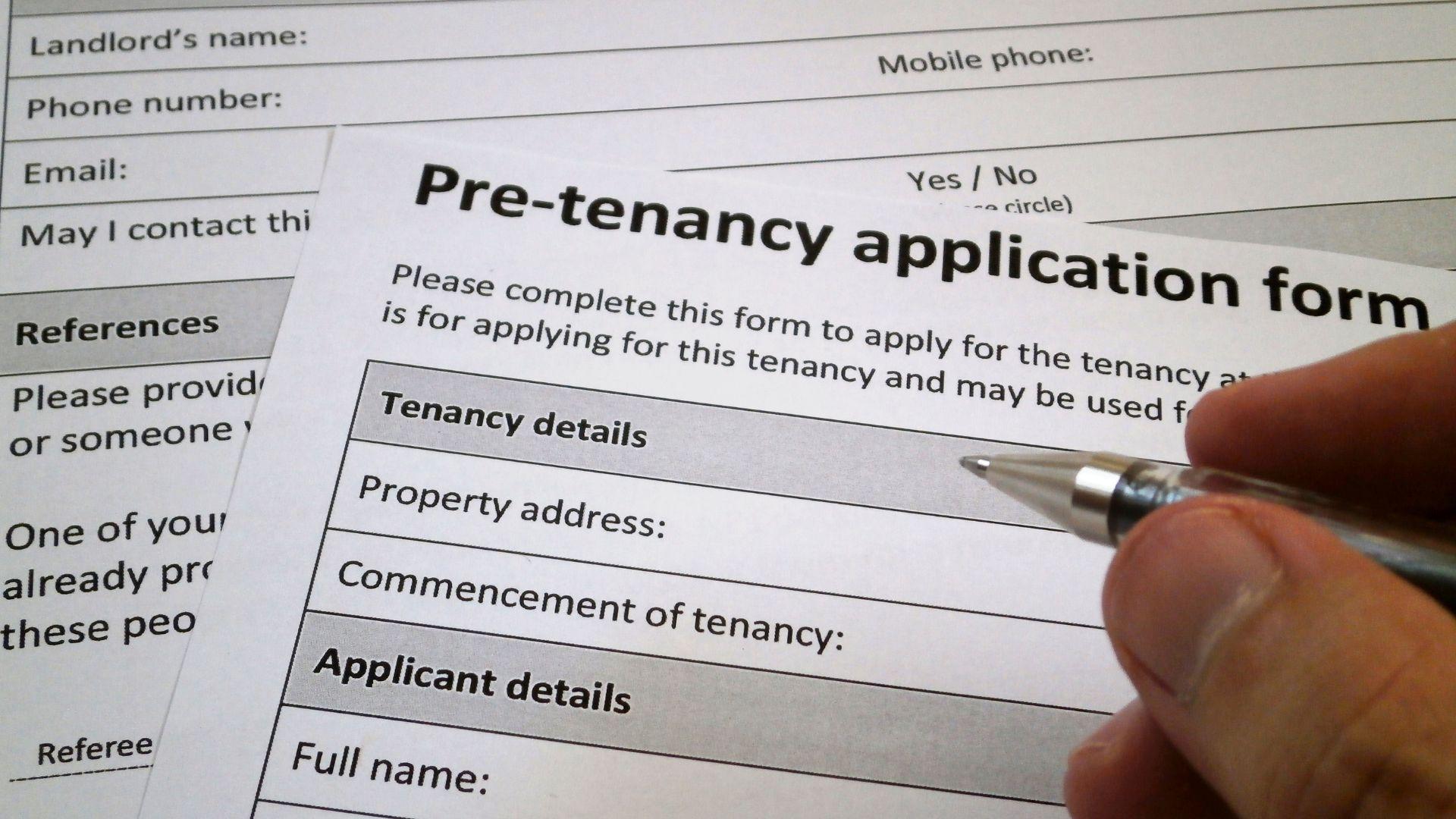 Close-up of an applicant filling out a paper pre-tenancy application form, representing the start of a rigorous tenant screening process.
