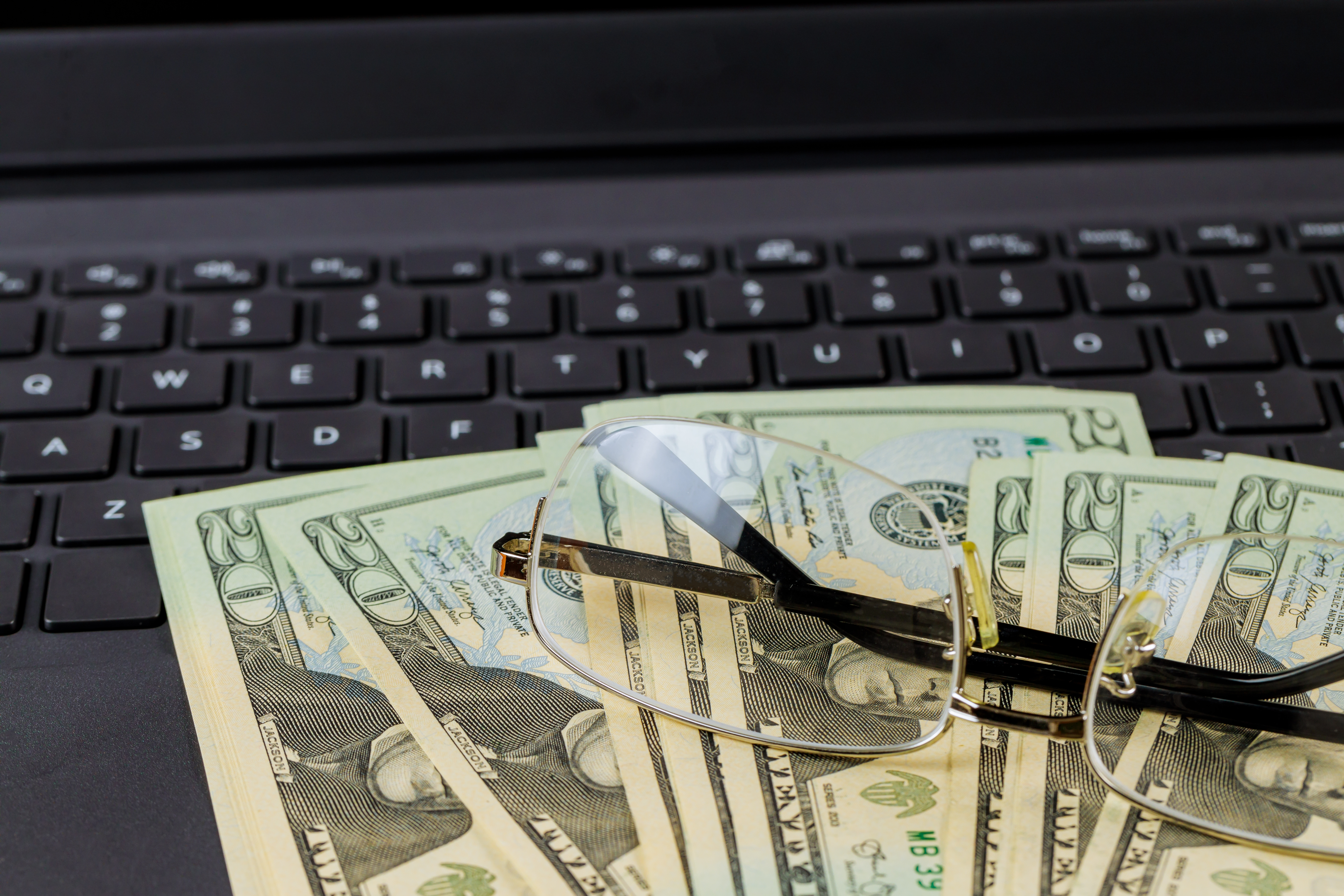 Money and eye glasses sitting on top of a laptop