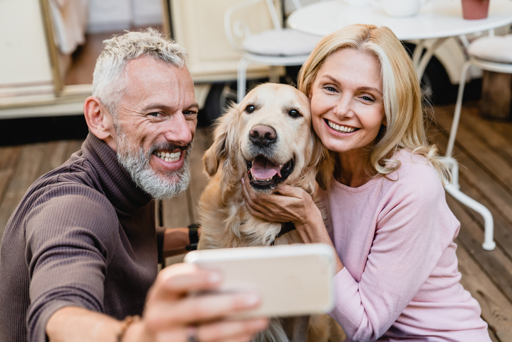 Happy blonde couple snapping a selfie with their dog.