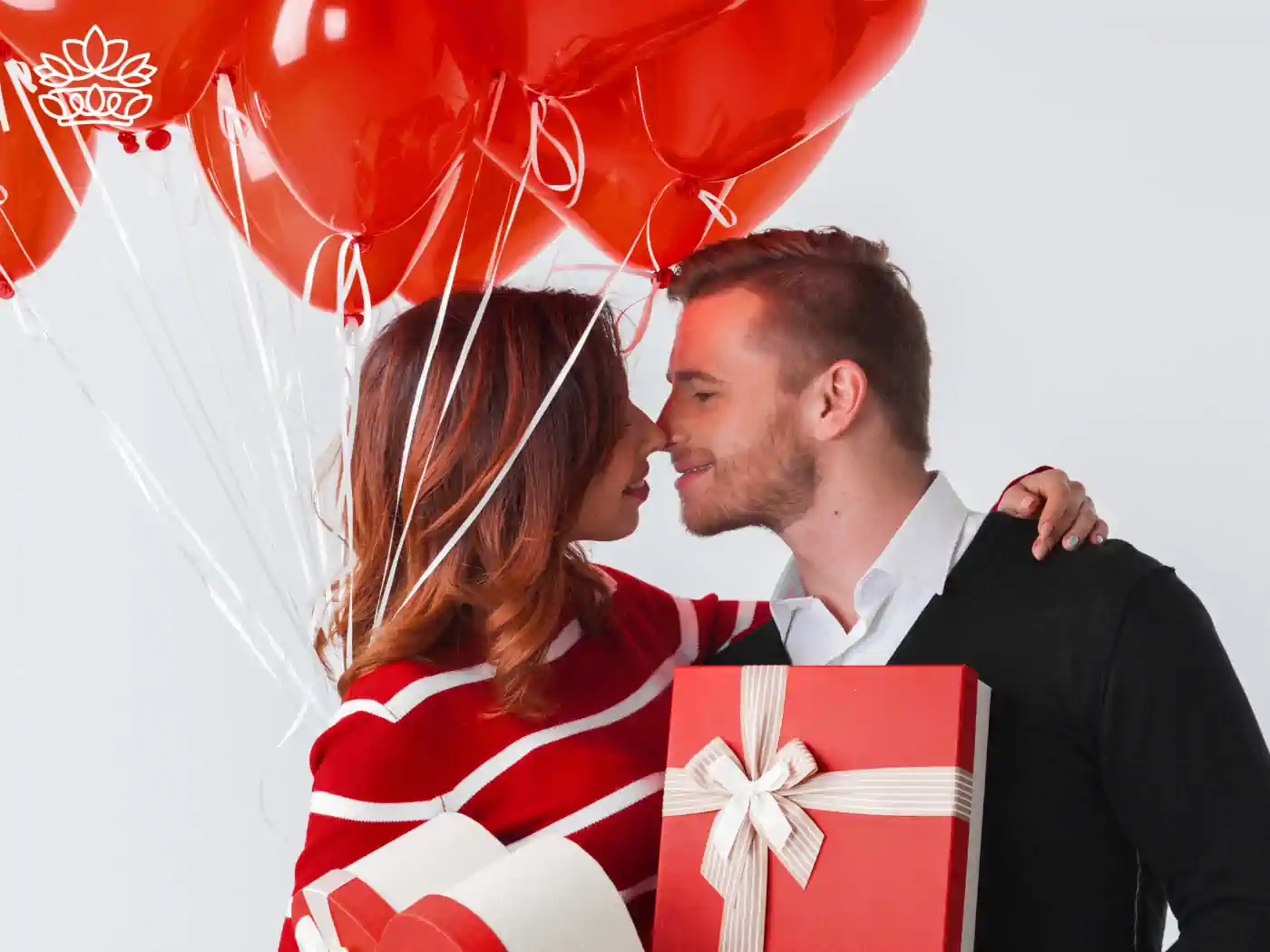 Affectionate couple with Valentine's Day red balloons and a large gift box, sharing a romantic moment. Fabulous Flowers and Gifts.