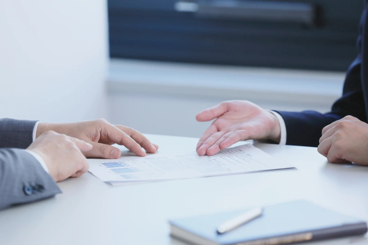 Hands gesturing over a document on a table with a notebook and pen in the foreground.