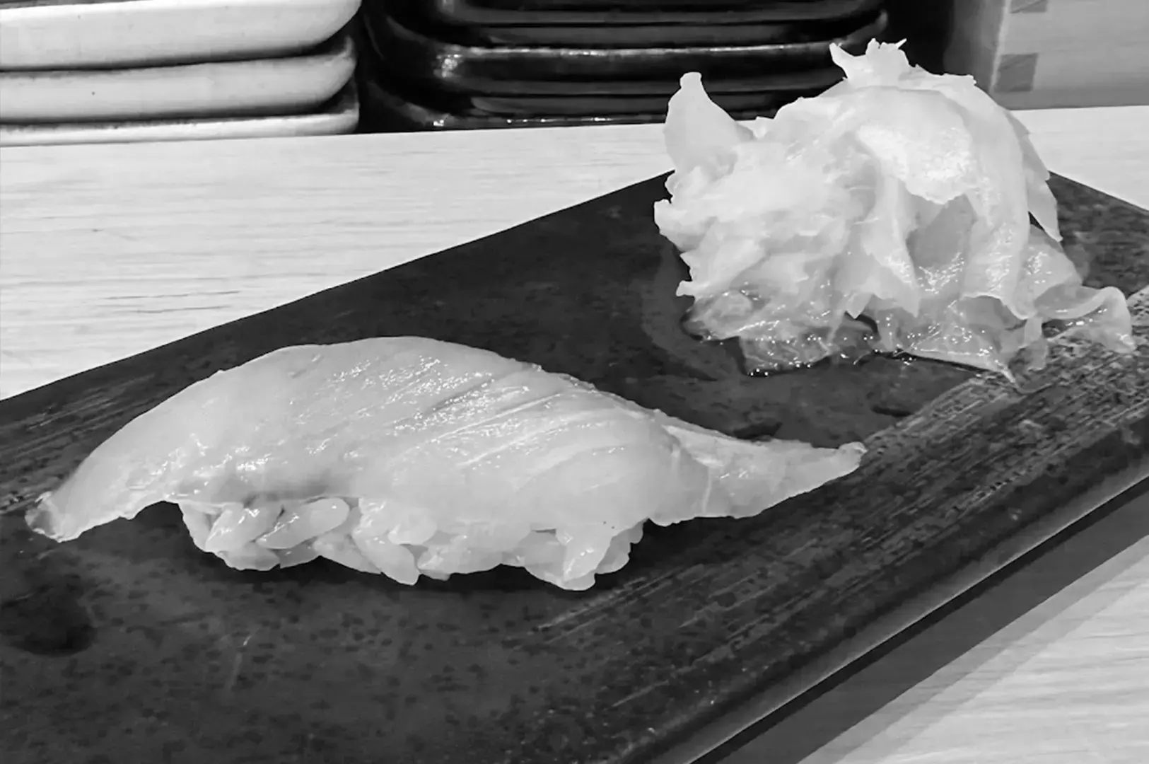 Close-up of nigiri sushi served on a dark rectangular plate with sliced garnish on the side.