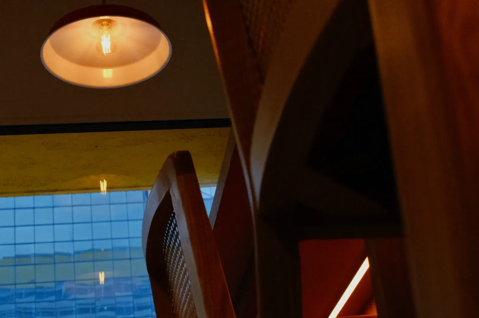 A low-angle view of wooden chairs with a light fixture overhead and a window showing reflections from a building outside.