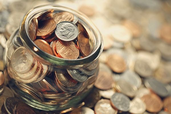 słoik pełen drobniaków, wokół niego leżą rozsypane pieniądze