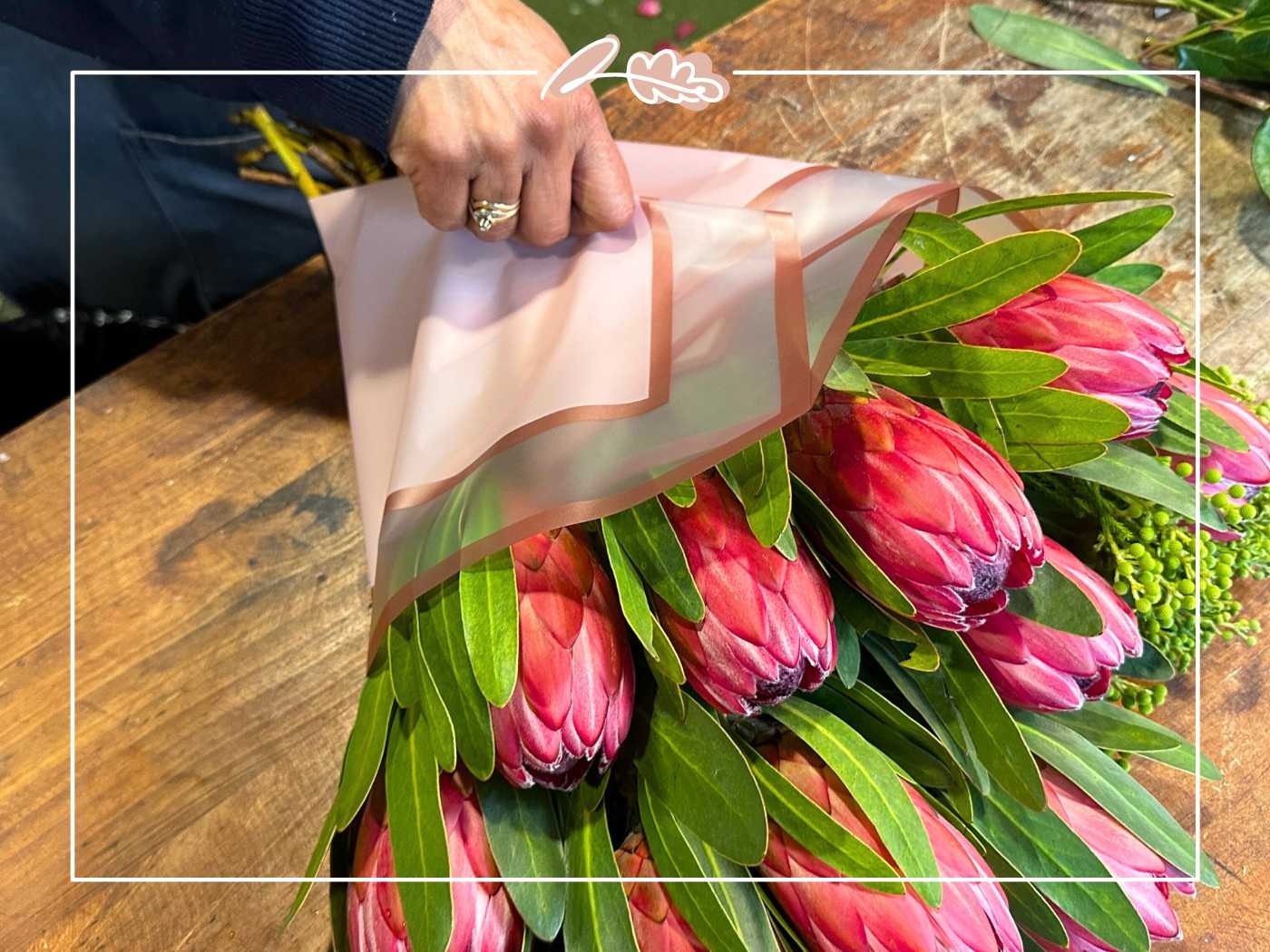 A florist's hands carefully wrapping a bouquet of pink proteas with brown paper - Fabulous Flowers and Gifts