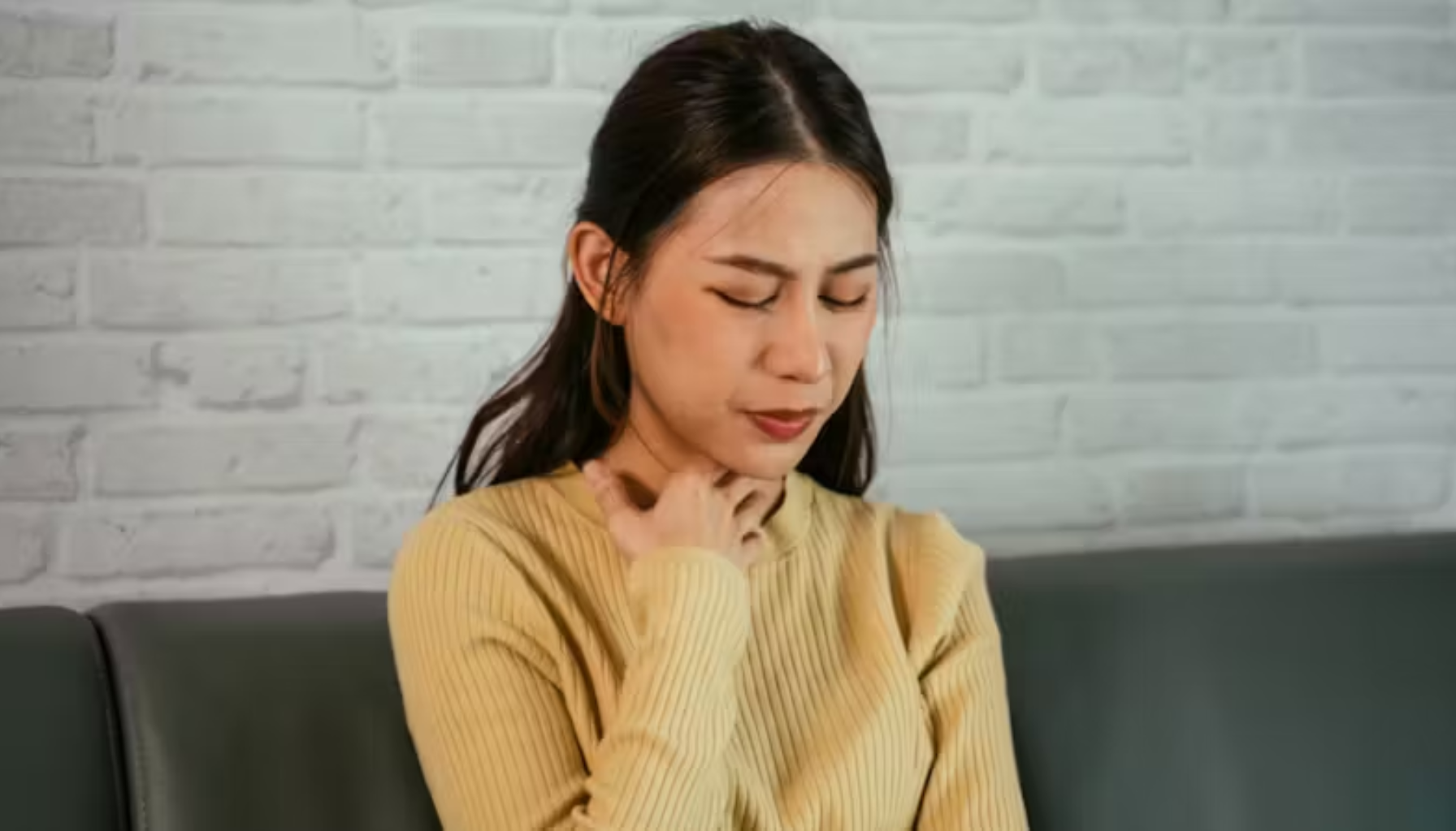 Tørr i Halsen: Når Problemet Starter i Munnen 13 Kvinne sitter på sofa og holder seg på halsen, uttrykker ubehag eller smerter i svelget.