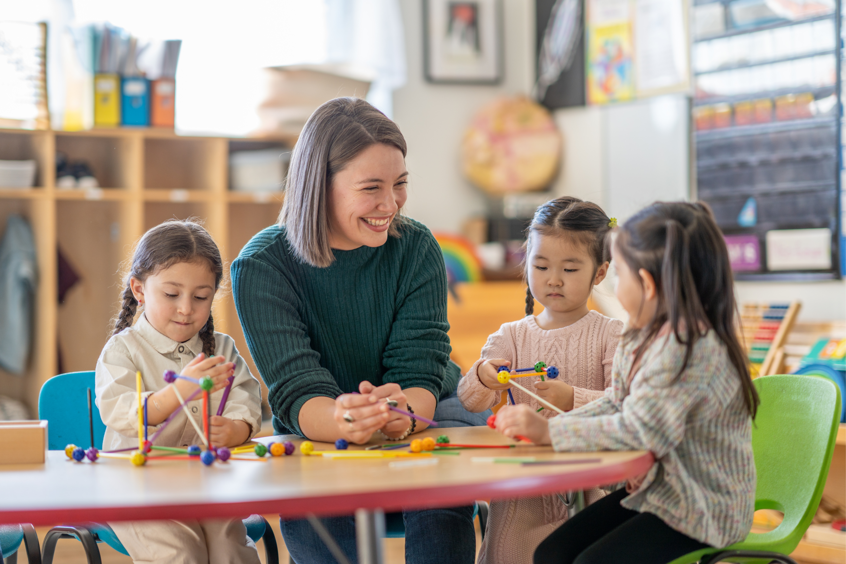 teacher smiling at table with preschool students 