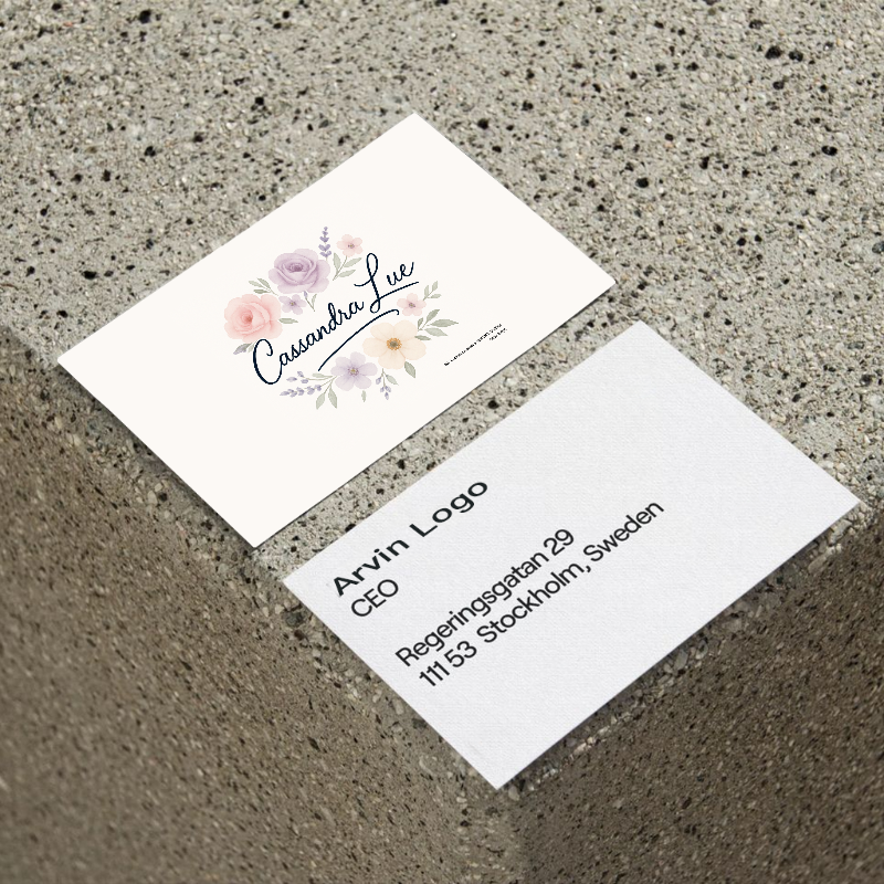 Two business cards placed on a speckled concrete surface. The top card features the name “Cassandra Lue” in elegant script, surrounded by pastel-colored floral illustrations.