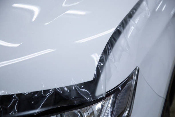 Paint Protection Film (PPF) sheet carefully positioned on a car’s hood, ready for application before smoothing and wrapping.