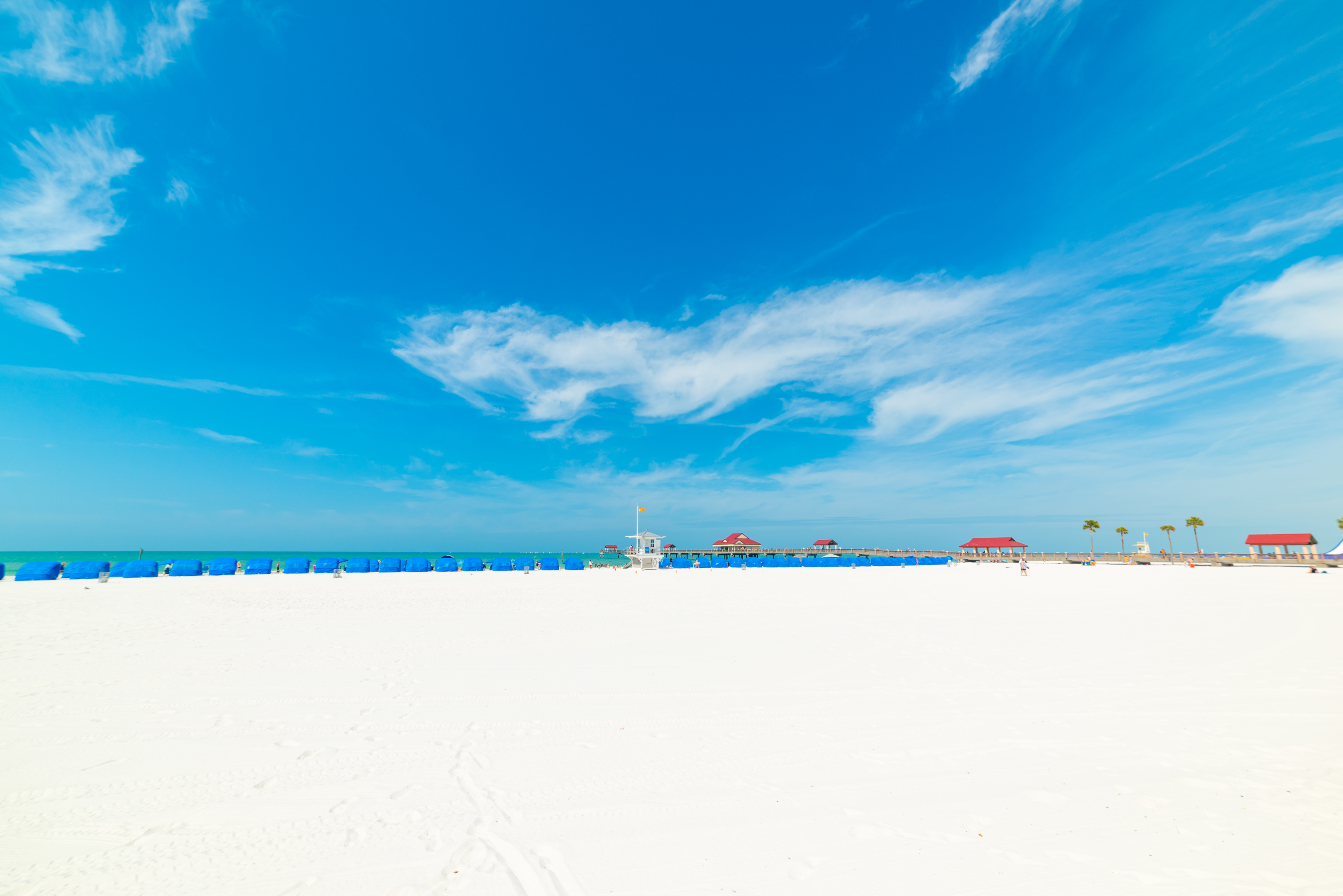 Clearwater Beach with white sand, blue skies, and blue beach chairs and people by the shore