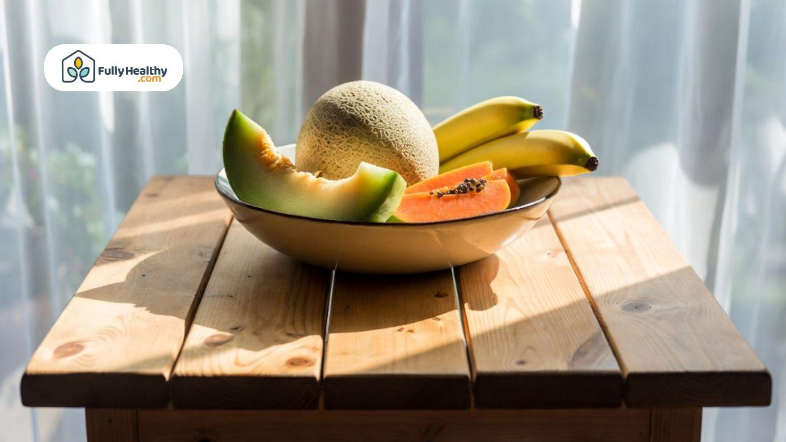 Bananas, melon, and papaya in a bowl on a wooden table with natural light.