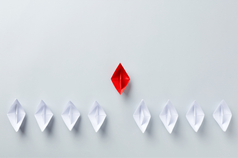 One red origami boat among white boats, representing a unique startup idea