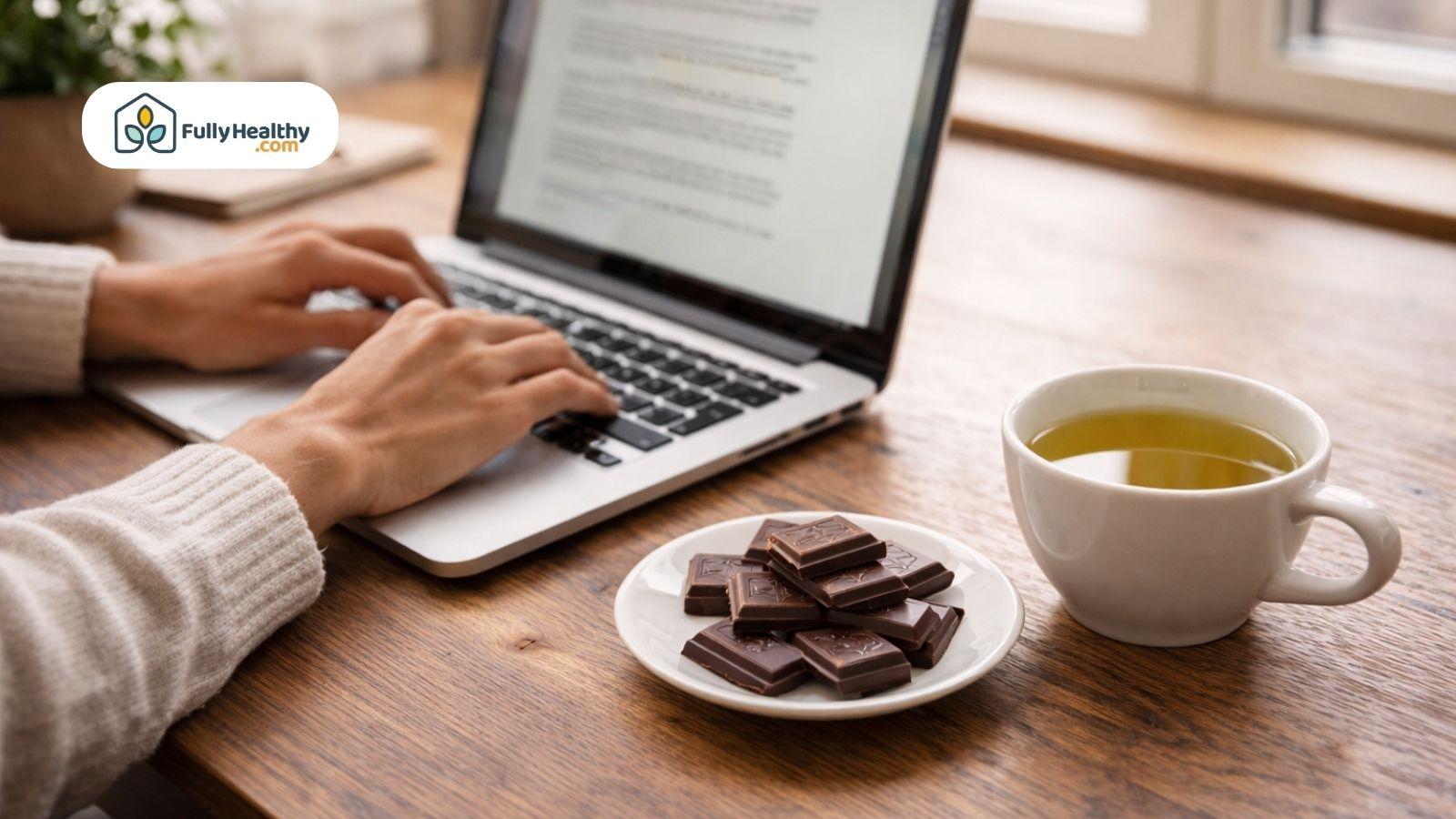 Person working on laptop with dark chocolate and green tea nearby