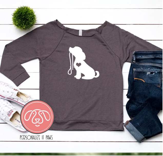 Long sleeve T-shirt, printed with a dog holding a leash. Jeans and shoes sit beside it on a table.