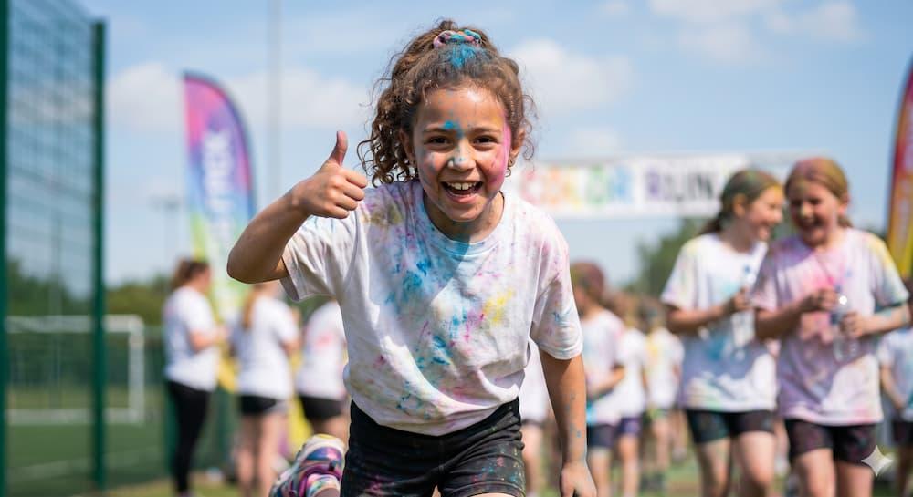 Smiling elementary school student covered in bright powder during a fun walk a thon fundraiser.