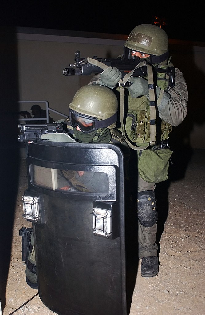 Two military personnel using a ballistic shield in a combat situation