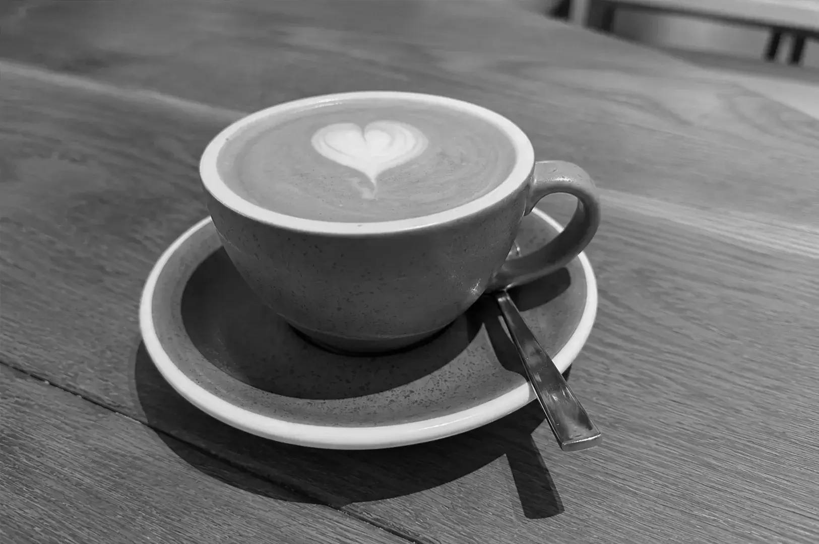 Side-angle view of a heart latte in a gray ceramic cup resting on a wooden café table.