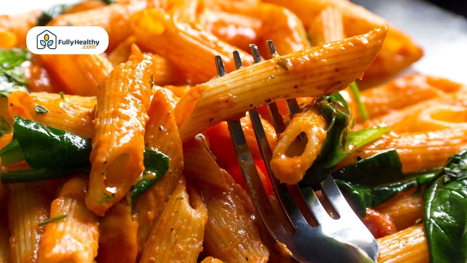 Fork lifting penne pasta with spinach and tomato sauce