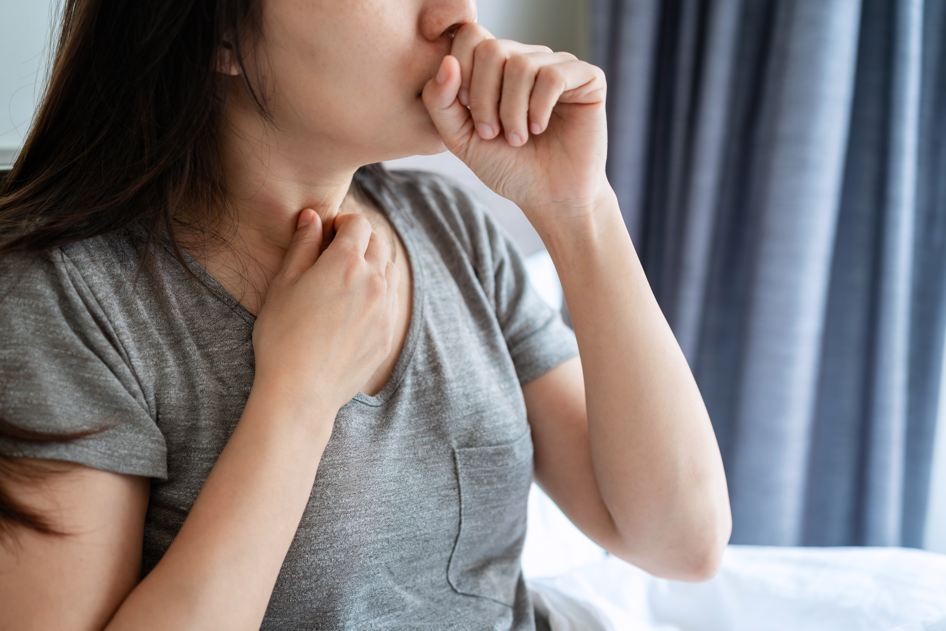 An image of a young woman feeling her throat and coughing into her fist. 