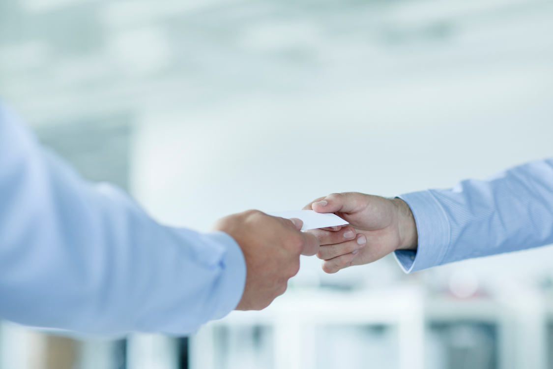 Close-up of two professionals exchanging a business card, illustrating a personal broker referral for a broker sourcing comparison.