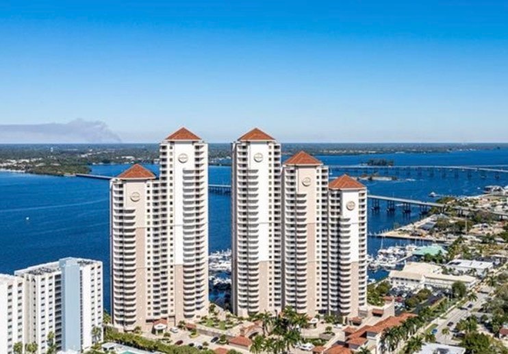 A tall luxury residential tower, known as High Point Place, rises majestically above the Caloosahatchee River, offering breathtaking views of the downtown Fort Myers skyline in the background. This impressive high rise features resort-style amenities and is situated in an urban waterfront setting, perfect for enjoying the vibrant Fort Myers River District.