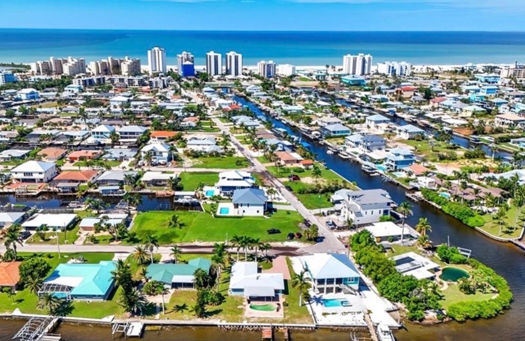 The image depicts a peaceful community street in Fort Myers Beach, showcasing beautifully designed coastal architecture surrounded by mature landscaping. This serene setting reflects the inviting ambiance of Fairview Isles, perfect for those seeking a tranquil lifestyle near pristine beaches and leisure activities.