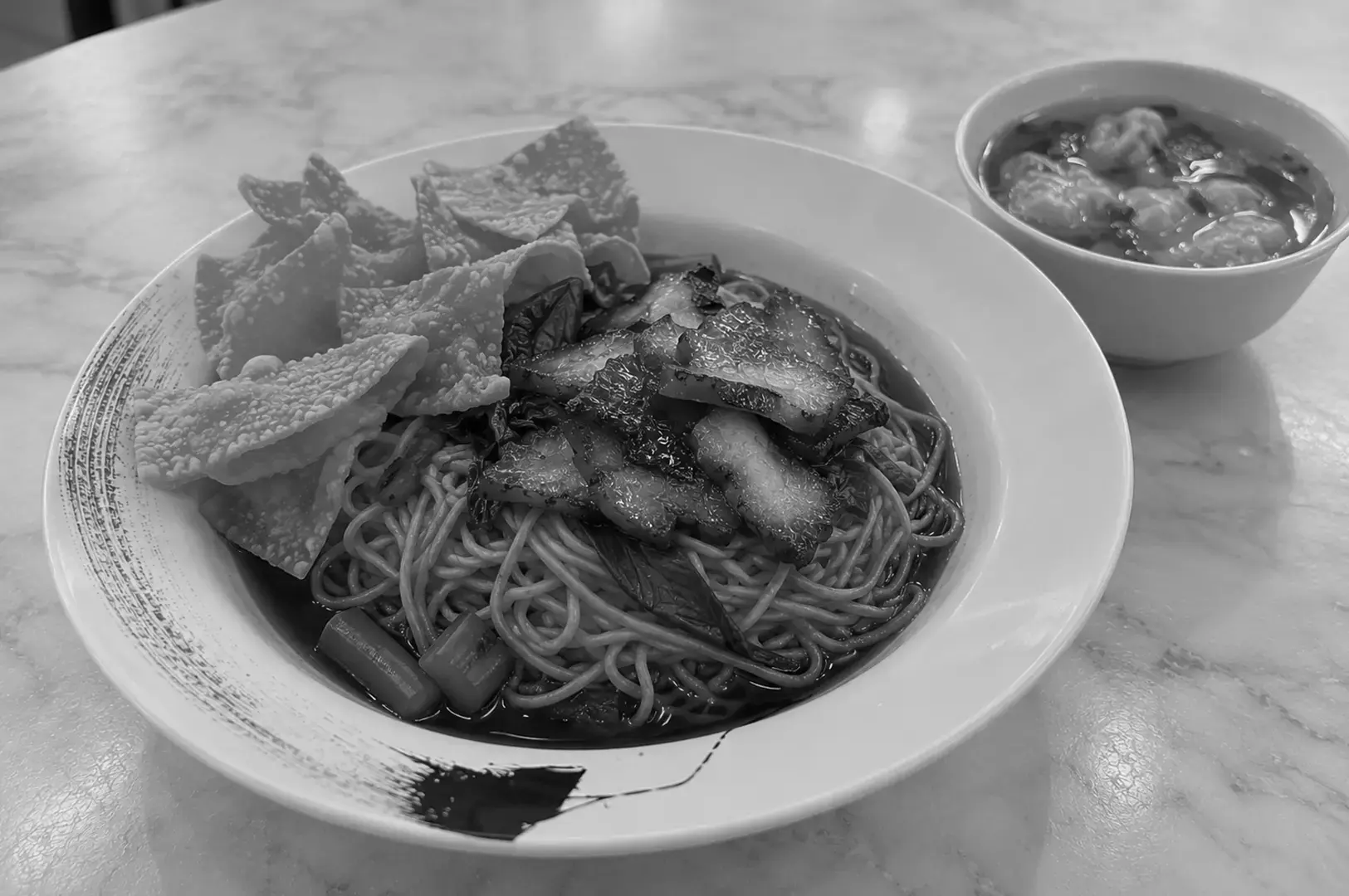 Wanton mee with egg noodles, roast meat, and dumplings arranged in a bowl with a side of soup.