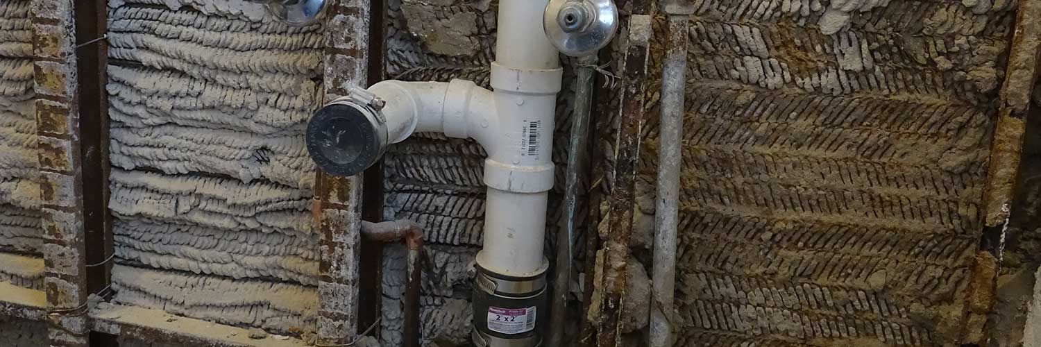 Drain and vent pipe for bathroom sink in old building. New pvc section replaced rusted metal; notice old concrete wall construction with no drywall wallboard or stud.