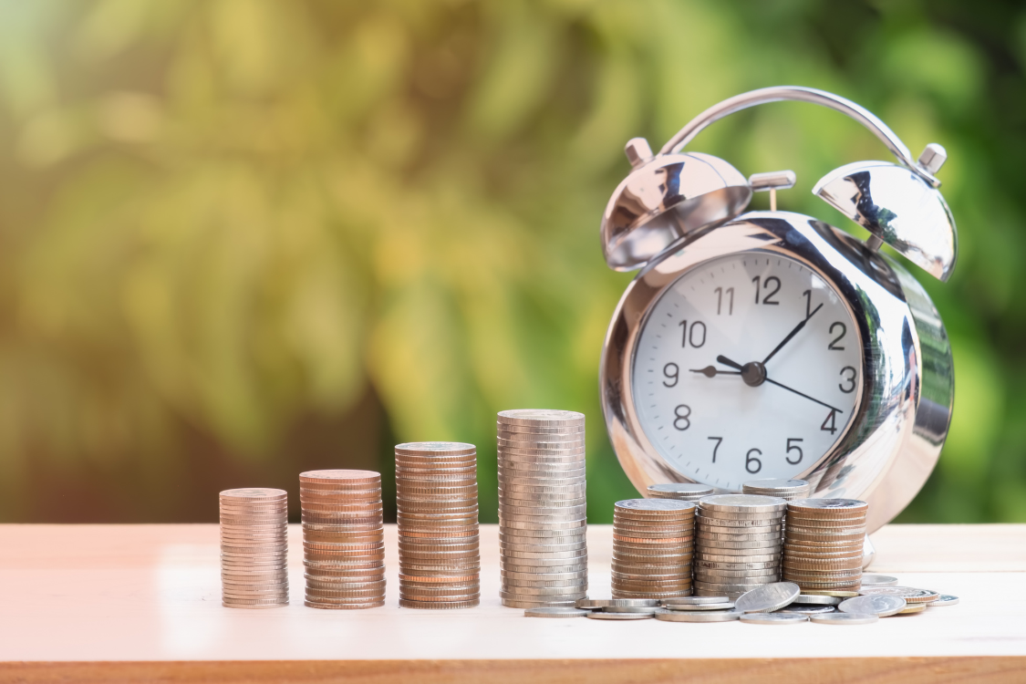Stack of coins beside an alarm clock symbolizing cost savings and time efficiency