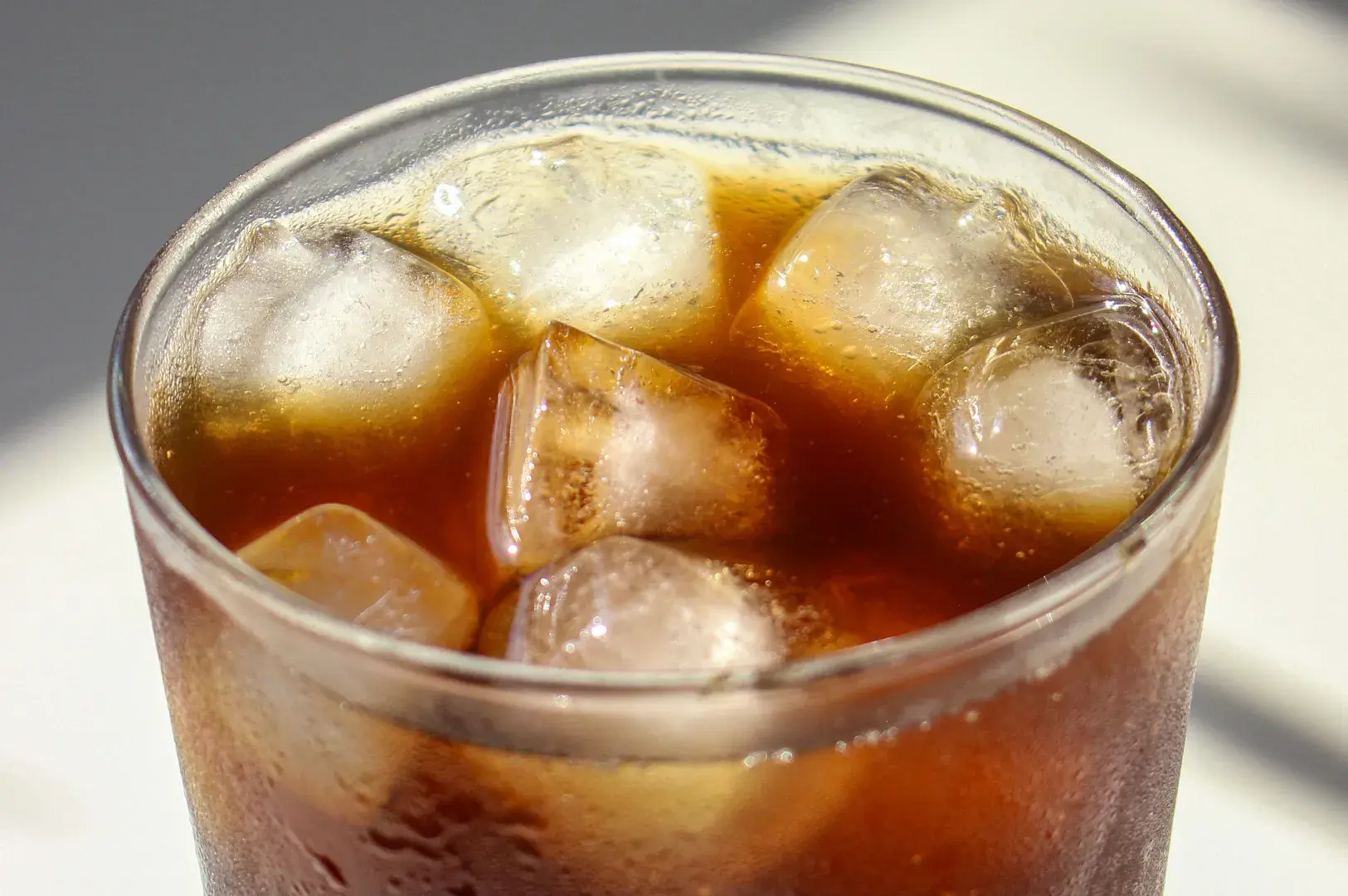 Close-up top-down view of a glass of tea filled with square ice cubes.
